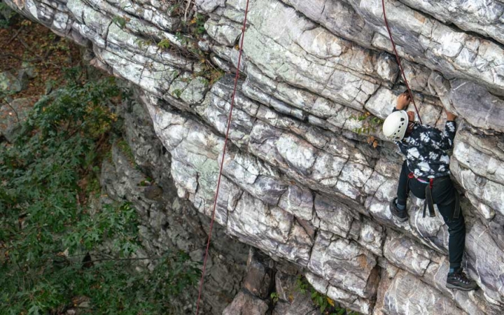 a teen scales a rock wall on a rock climbing trip with outward bound